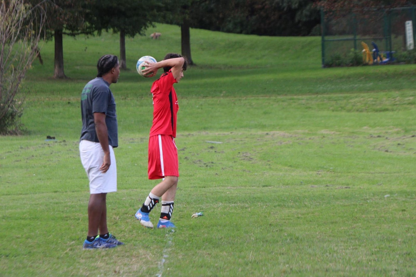 A coach stands beside a young player taking a throw-in